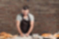 baker-wearing-apron-kneading-dough-kitchen-counter-standing-against-brick-wall.jpg