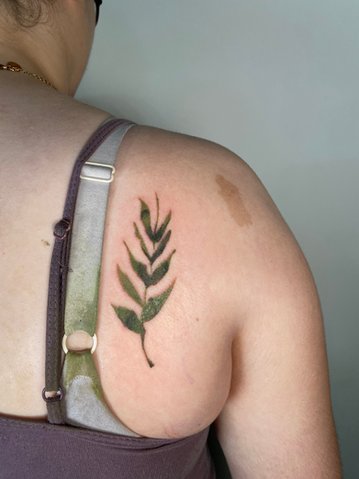 Watercolor-style green leaf tattoo on upper back