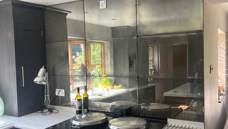Foxed antique mirror wall panels by Mirror Works installed behind cooker, handcrafted and toughened for safety and style.