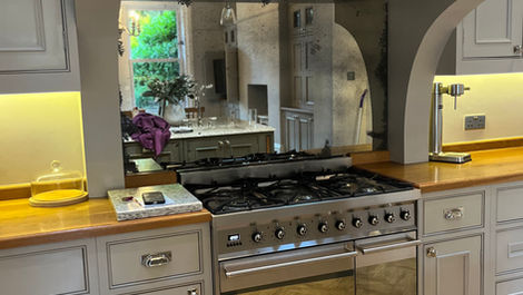 Rustic kitchen with vintage-style aged mirror glass splashback above a stainless steel range cooker, created by Mirror Works.