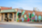 Brick building with vibrant floral mural and text "She believed she could, so she did." Signs read "Market on Main" and "LIFE Choices."