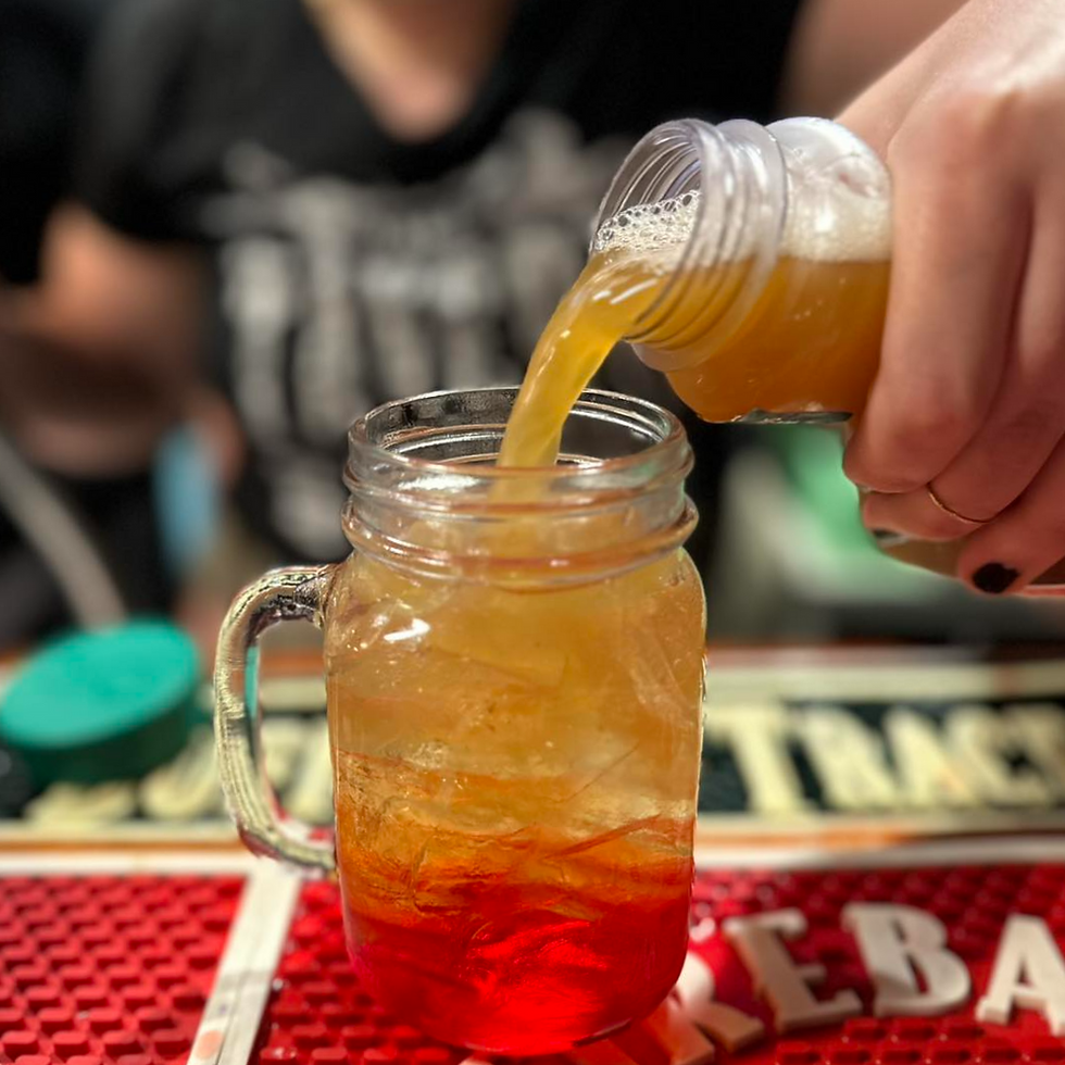 A hand pours amber liquid into a mason jar with red liquid on a bar mat. Blurred background. Energetic mood.