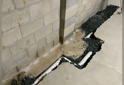French Drain Installation of a PVC pipe in a dug-out trench in a basement with 3/4" blue stone