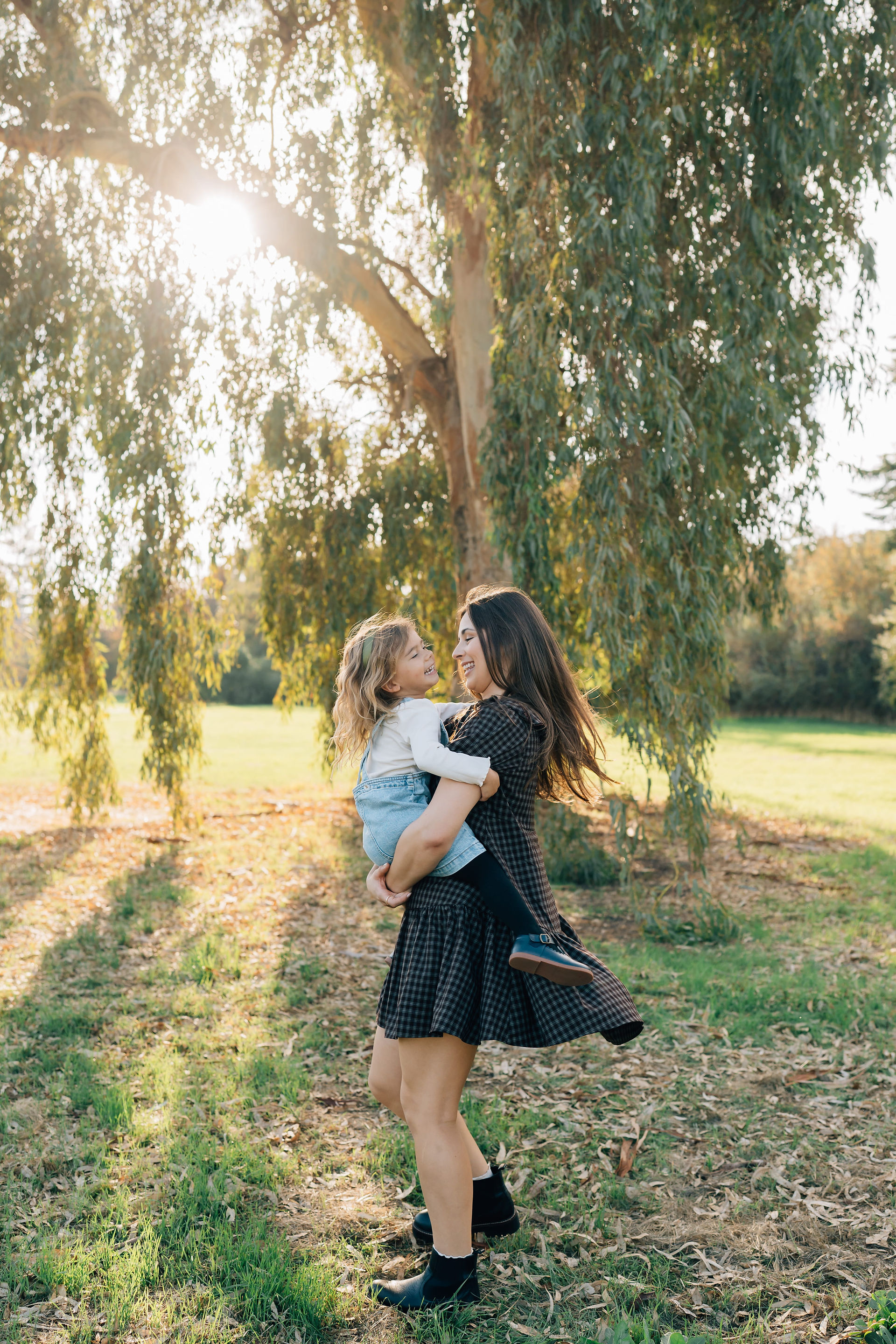 A mom holding her daughter by a willow tree during sunset