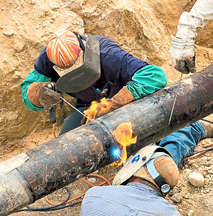Two men with welding helmets welding a pipe