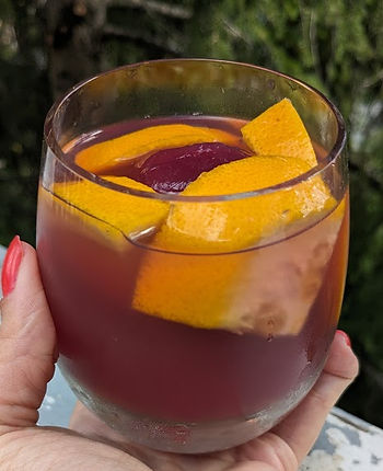 A hand holding a glass containing hibiscus tea and orange wedges