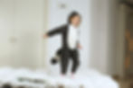 A child dressed in a raccoon costume jumping on a bed