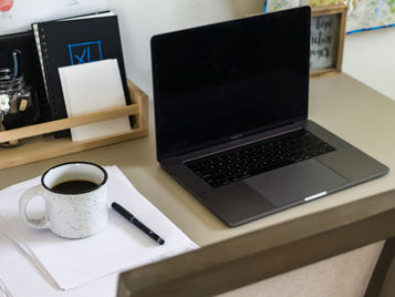 Arbeitsplatz mit Laptop, Notizbuch und Kaffeetasse als Symbol für die Entstehung persönlicher Führungsimpulse in entspannter Atmosphäre.