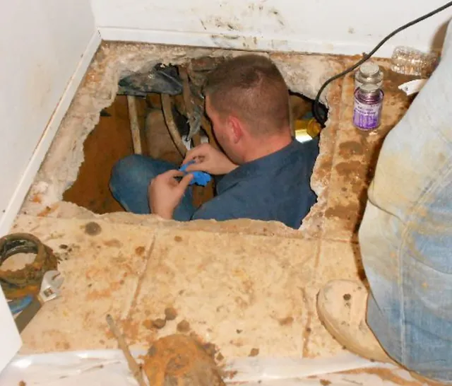 plumber-under-broken-flooring-repairing-pipes