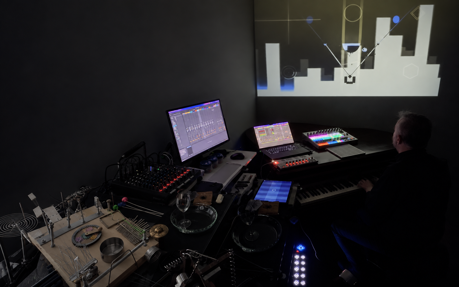 Composite of monomelist seated at the piano, with custom instruments and projected visuals throughout his studio.