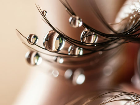 Close-up of a person's eye with a single tear resting on the eyelashes.