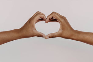 Two hands join together to make the symbol of a heart in front of a light grey background