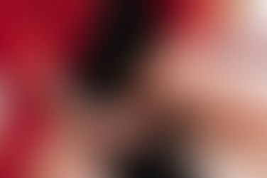 A woman kneeling on a white shag rug on the ground, wearing a red robe and black dress, holding pills in her hand.