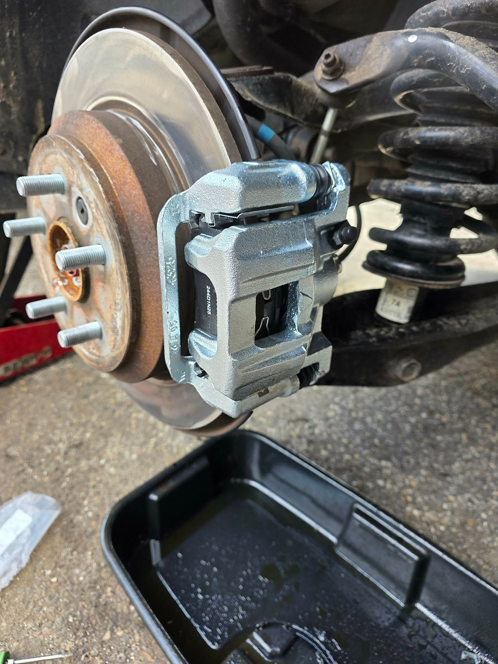 New silver brake caliper and brake pads installed on a vehicle rotor during a professional brake service
