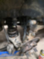 Professional suspension repair showing disassembled wheel hub and shocks on a vehicle lifted by a floor jack