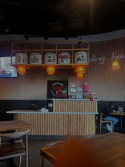 Restaurant interior with counter and decorations; Sizzling House & Rice Noodles 1 in background.