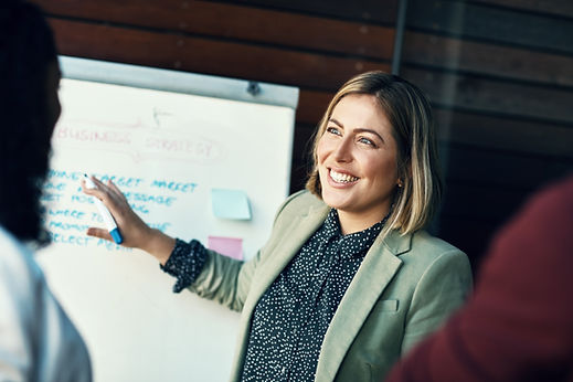 A woman in a blazer presenting at a whiteboard covered in sticky notes