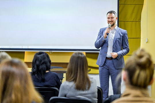 A man presenting with a microphone to a seated audience in a lecture room.