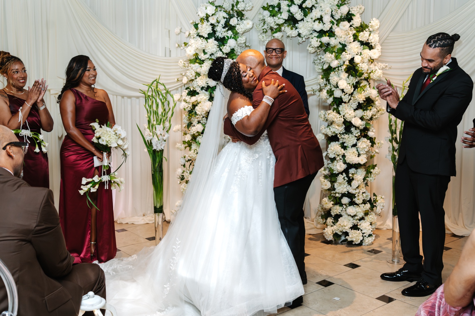 Ramarra and Evan kissing beneath a white floral arch at Laurel Manor in Livonia.