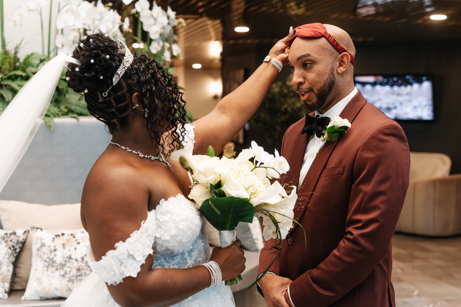 Ramarra holding a burgundy cloth to Evan's forehead during a candid wedding moment.