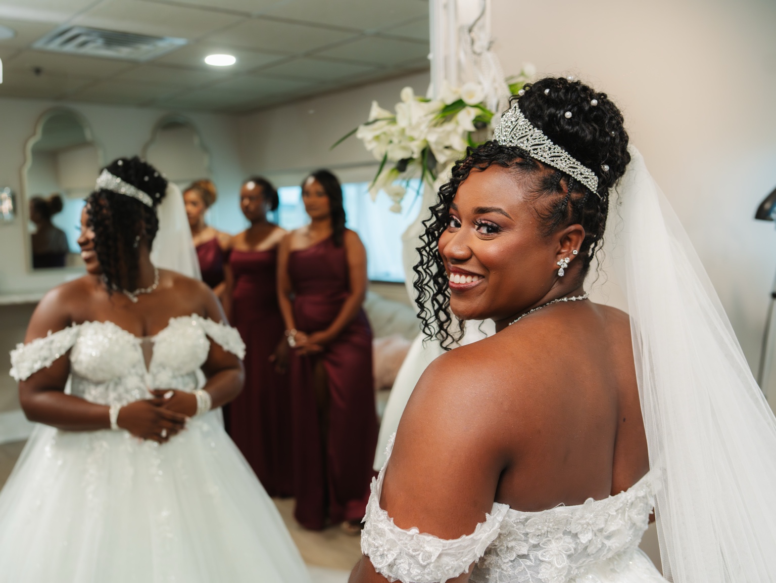 Ramarra beside a mirror with her bridesmaids reflected behind her.
