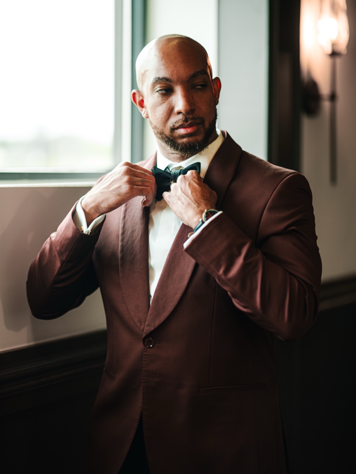 Evan adjusting his bow tie in a burgundy tuxedo.