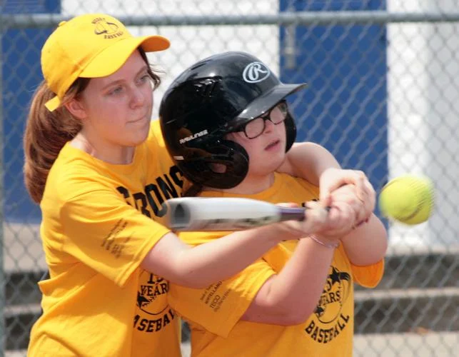 A Buddy Baseball player helps a player with special needs bat during a game. 