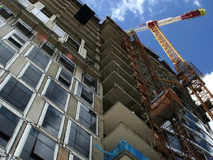 A high-rise development rises skyward, cranes and scaffolding punctuating the clear blue expanse.