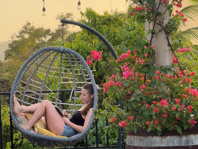 woman sitting in a swing chair writing with a beautiful sunset surrounded by flowers