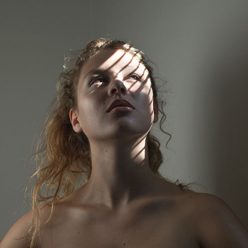 Femme aux cheveux bouclés, visage levé, traversée de rayons de lumière sur fond gris