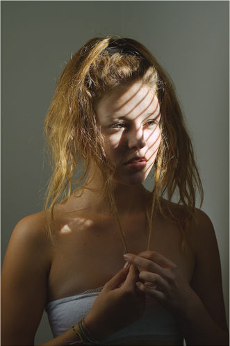 Femme aux cheveux longs, visage strié d'ombre et de lumière, mains jointes contre la poitrine