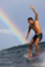 Male surfer nose riding a wave with a rainbow in the background in Siargao, Philippines