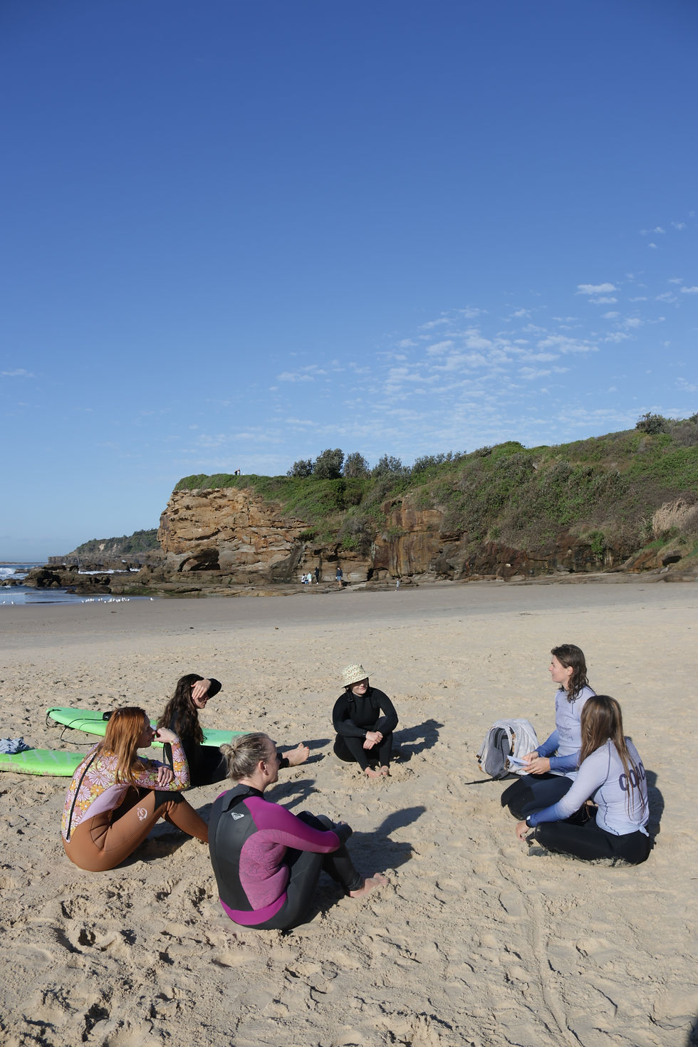 Women sitting on the beach listening to their instructor during a group surf lesson in Newcastle, NSW
