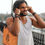 Thumbnail: A boho man with dreadlocks wearing white t-shirt walking outdoors with ear buds. A Mandala tote bag hangs from his shoulder.