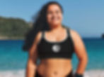 Plus size woman standing on beach smiling. She’s wearing a black OM symbol sports bra and black bikini bottom.