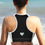 Thumbnail: Back view, yoga woman standing at edge of the ocean beach. She’s wearing a black Love Yourself sports bra.