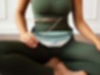 Yoga woman meditating, sitting cross legged wearing a sea green OM symbol belt bag around her waist, holding incense stick.