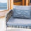 Thumbnail: 12”x20” Seagulls on a Bluff throw pillow (seagull flock side) on a wicker chair next to a window with a view of the ocean.