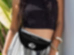 Fashionable boho girl wearing a black tank top, wide legged pants, and a black OM symbol belt bag around her waist.