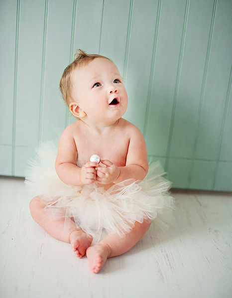 Blonde newborn sitting on the floor in her tutu with teal shiplap in the background