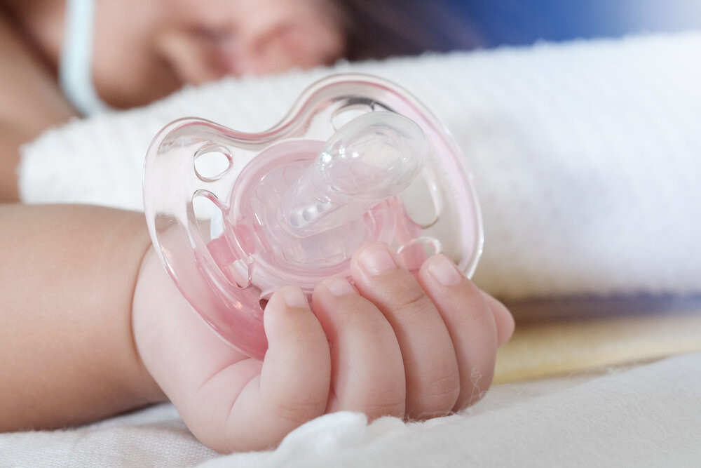 Hand of a sleeping baby holding a pacifier