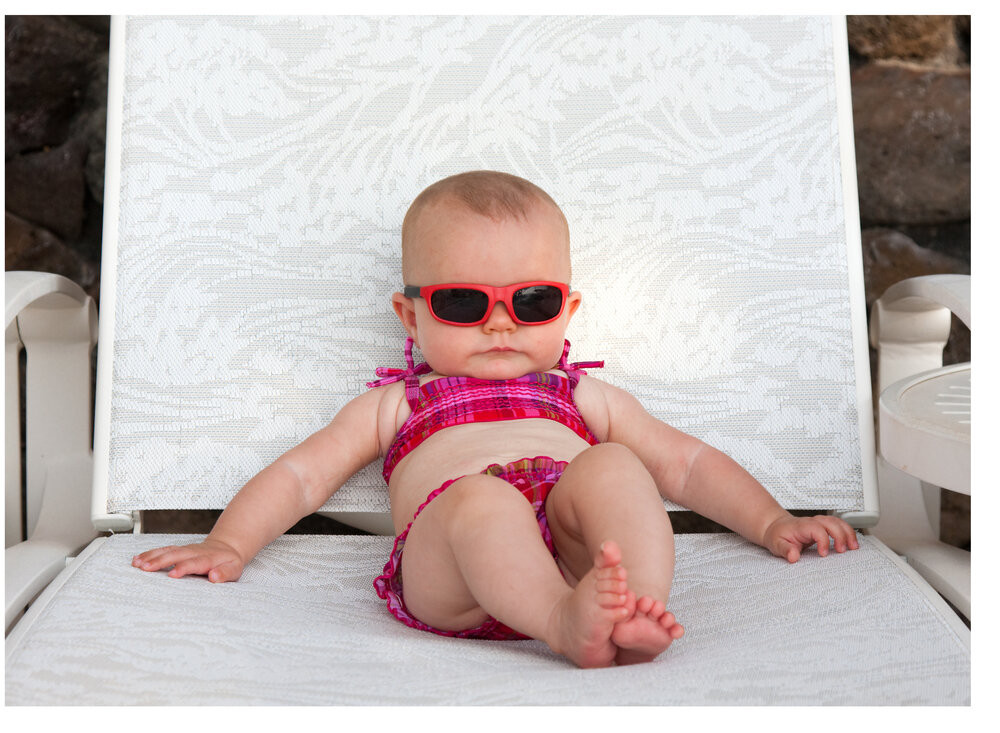 Toddler in a bathing suit and sunglasses lounging on a reclined pool chair