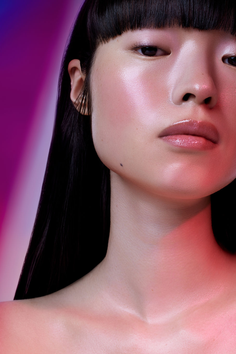 Model's face, neck and shoulders lit with deep purple and warm red gel light in a stained glass-inspired beauty editorial