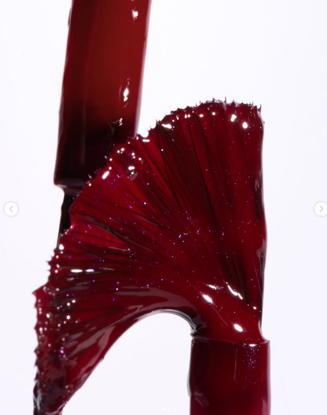 Kathrin Werner cosmetic texture photographer London — deep crimson nail polish brush pull, gel formula stretching into micro-thread fan with purple glitter, macro beauty photography for luxury nail brand