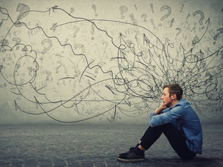 A young man sitting on the floor and random markings on wall depicting his spiraling thoughts