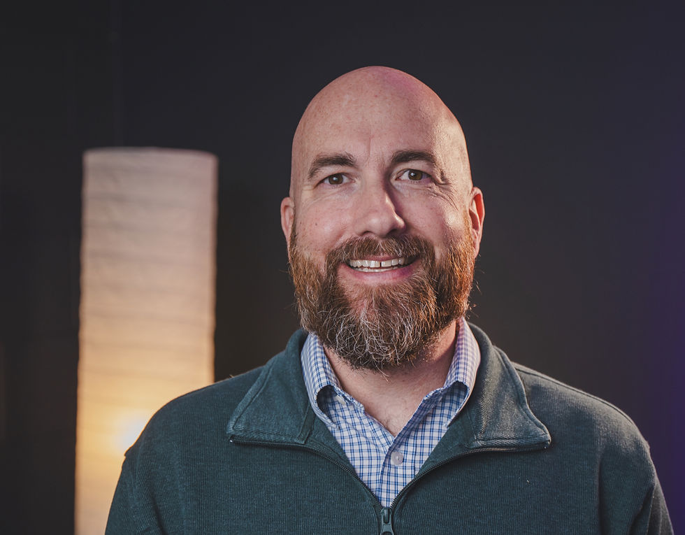 A man with a red beard wearing a gray sweater and blue shirt