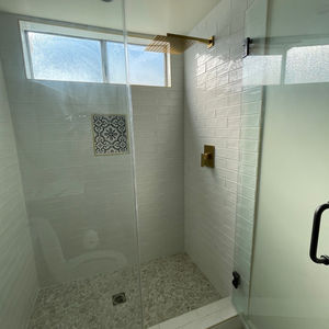 New walk in shower with frameless glass door and bronze hardware installed with shampoo niche. white tall shower walls