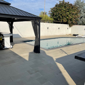 aluminum black pergola sitting in backyard in front of a newly built pool surrounded by freshly installed concrete pavers