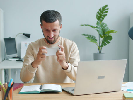 Office worker checking a smartphone while seated at a laptop