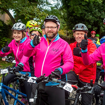 Cyclists lined up in pink kit with their thumbs up ready for the start of a ride.